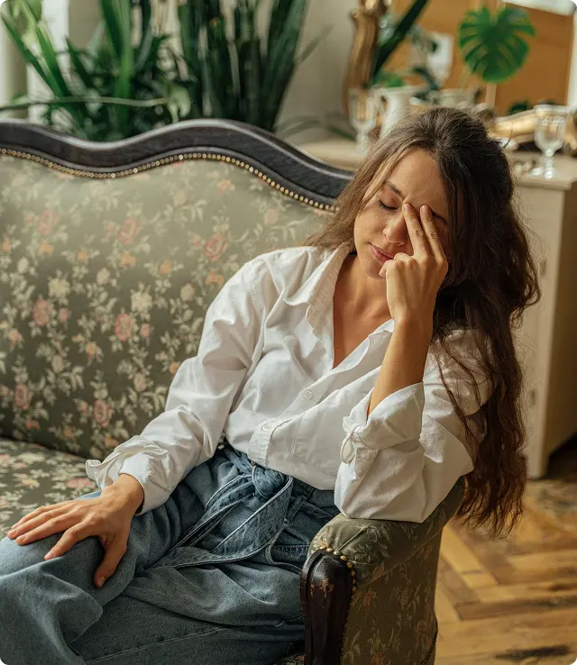A woman sits on a couch, her head resting in her hands, conveying a sense of distress or deep contemplation.