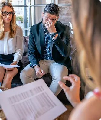 A man and woman sit on a couch, reviewing documents and papers together in a casual setting.